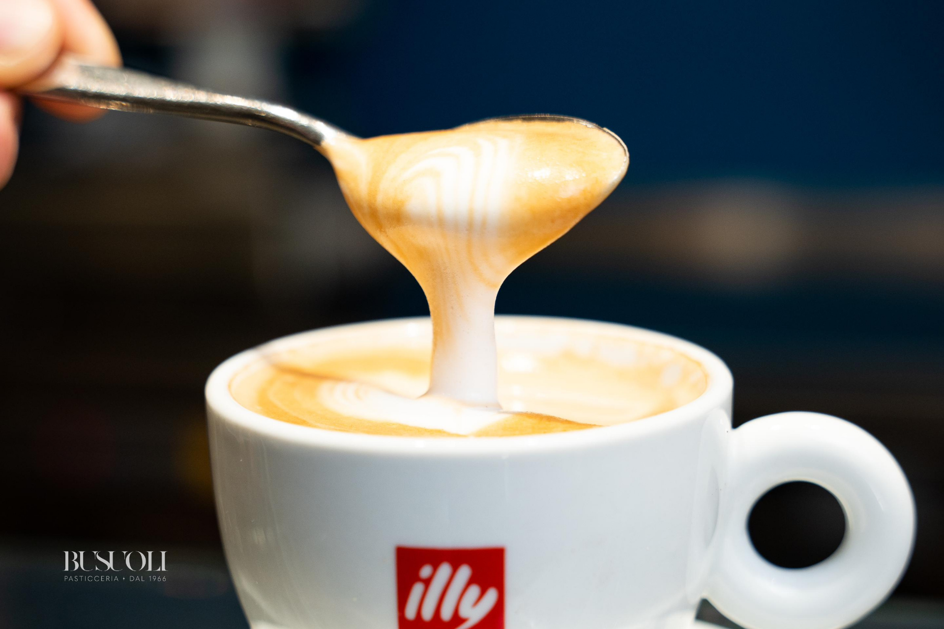 Un cucchiaino che solleva la crema del cappuccino con caffè Illy